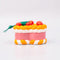 side view of ceramic pink cake shaped ornament with orange and white trim and 'cherries on top' 