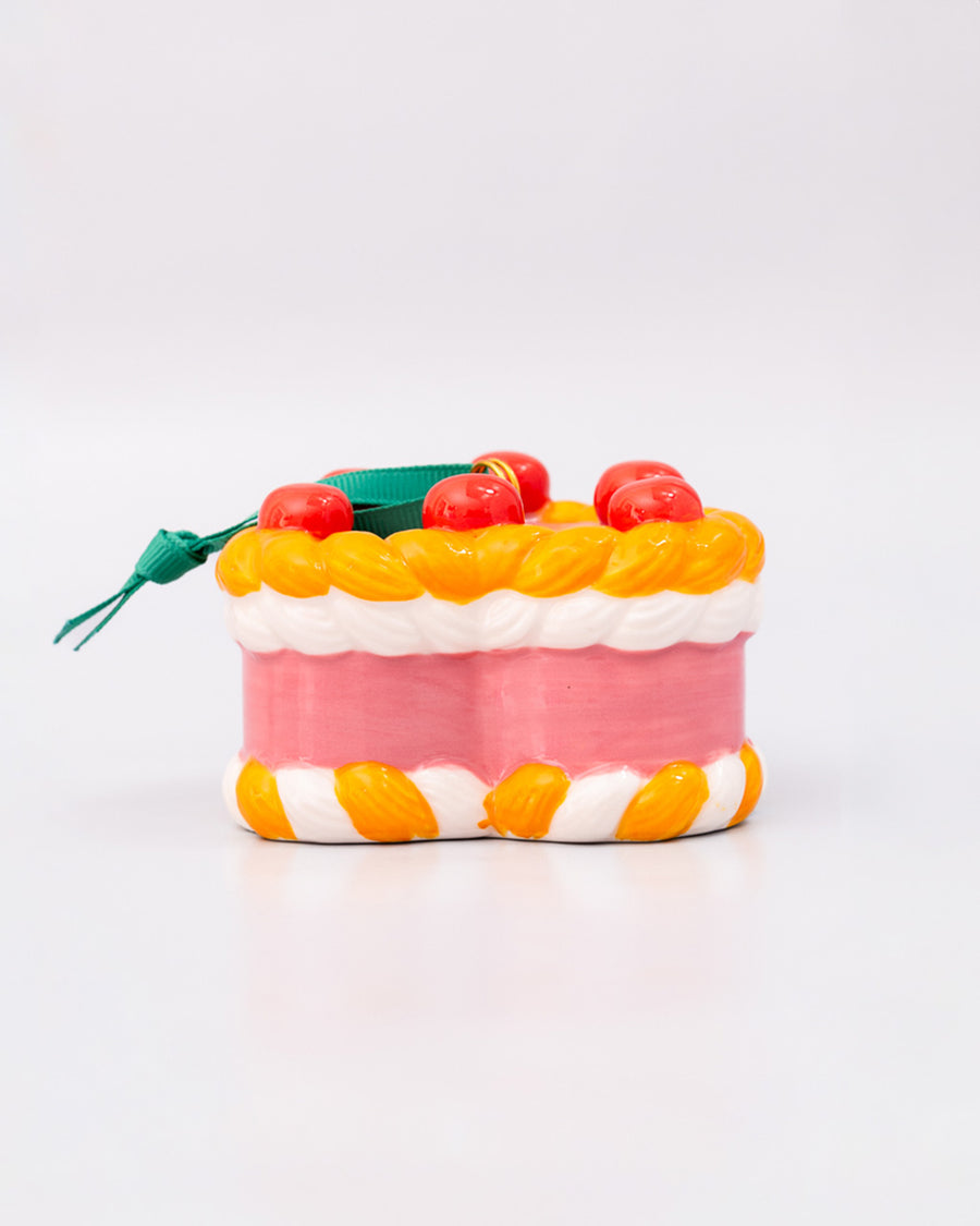 side view of ceramic pink cake shaped ornament with orange and white trim and 'cherries on top' 