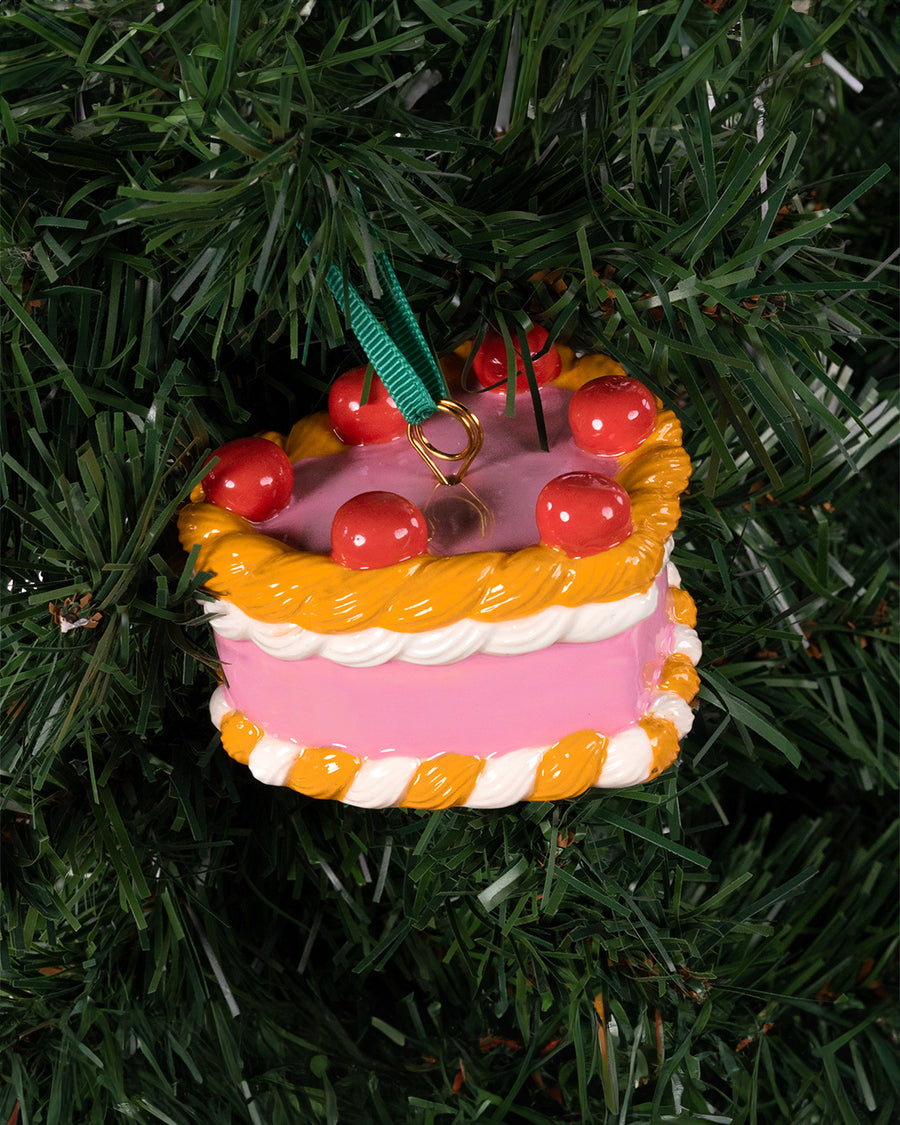 ceramic pink cake shaped ornament with orange and white trim and 'cherries on top' in a tree