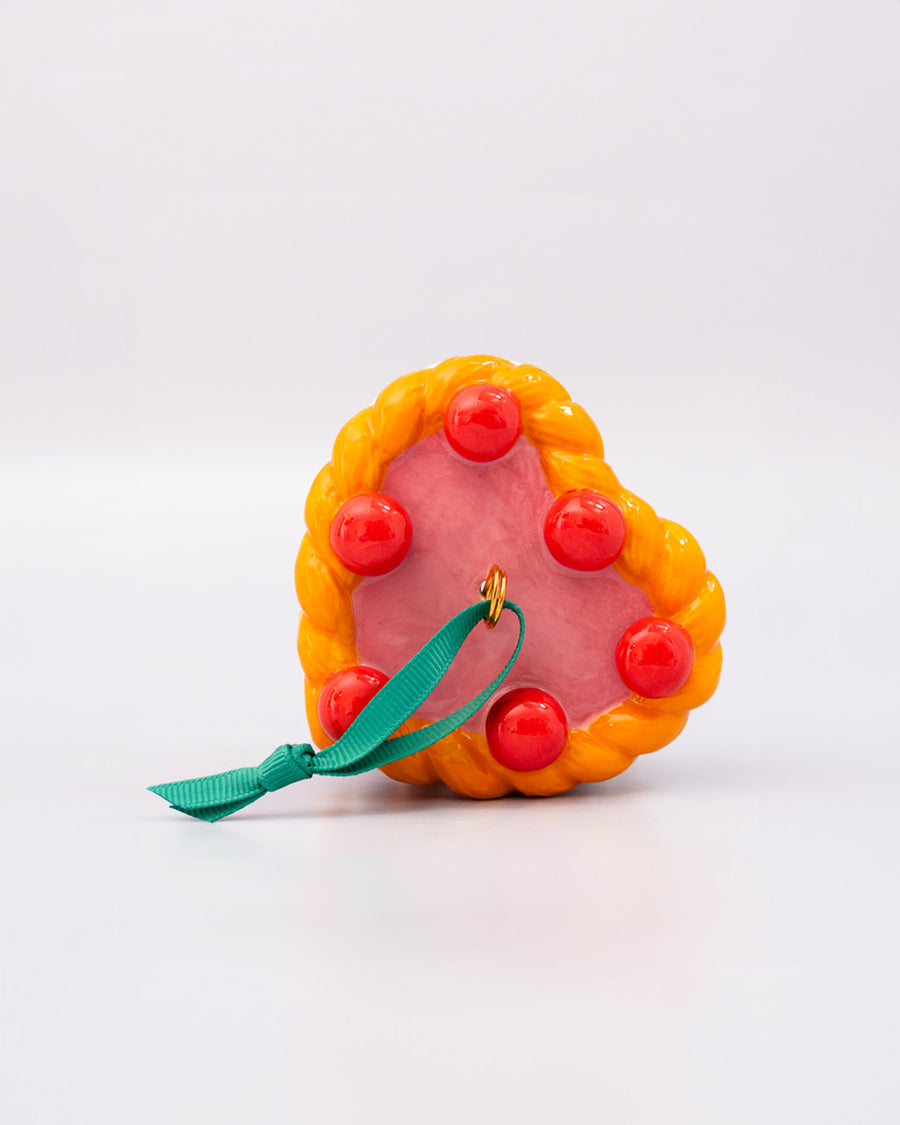 top view of ceramic pink cake shaped ornament with orange and white trim and 'cherries on top' 