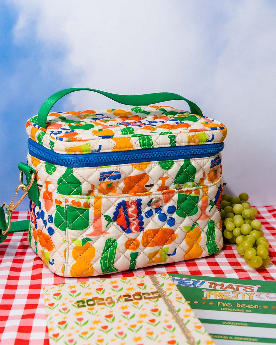 white quilted lunch bag with all over charcuterie print with green and blue trim on red and white checkered table cloth