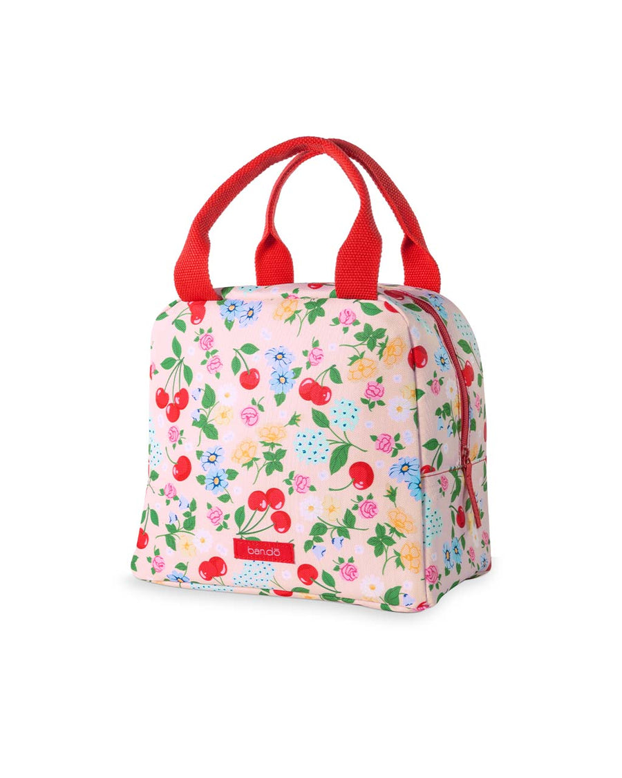 side view of light pink lunch tote with all over cherry and flower print and red handles