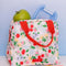 light pink lunch tote with all over cherry and flower print and red handles with lunch items inside