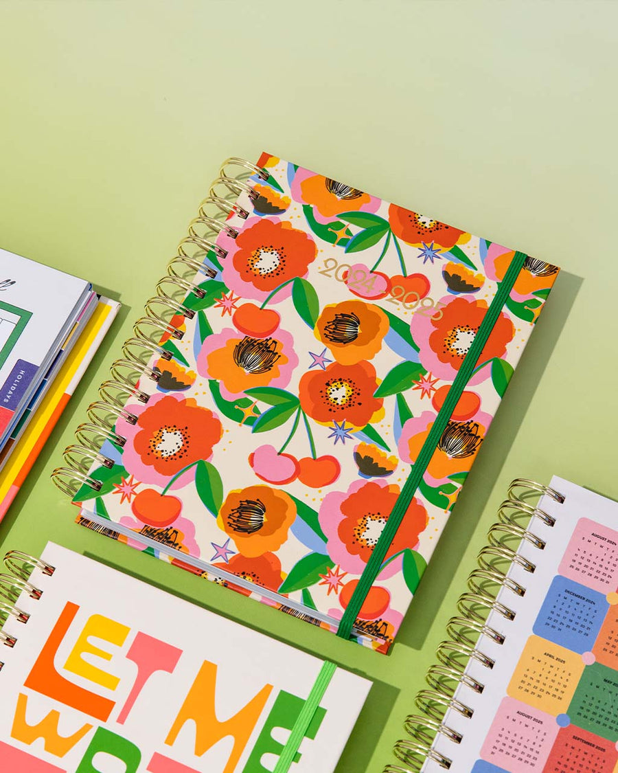 cream 17-month planner with colorful floral and cherry print surrounded by planners