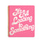 pink large notebook with white 'it's all leading to something' typography across the front