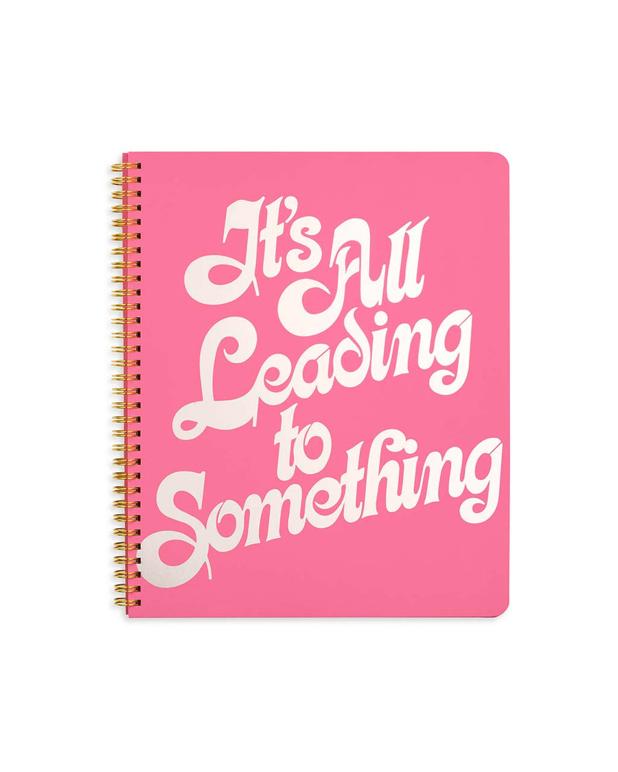 pink large notebook with white 'it's all leading to something' typography across the front