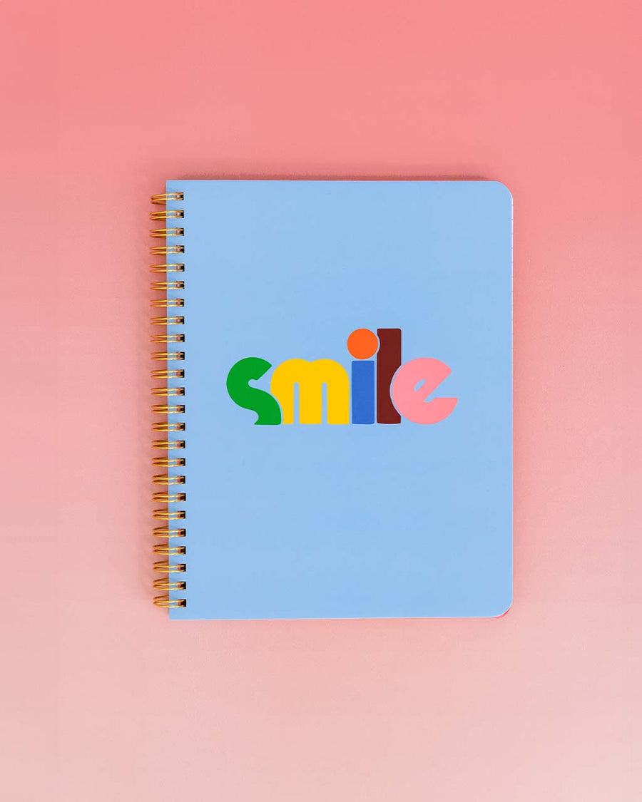 baby blue mini notebook with rainbow 'smile' typography across the front on red and white gradient ground