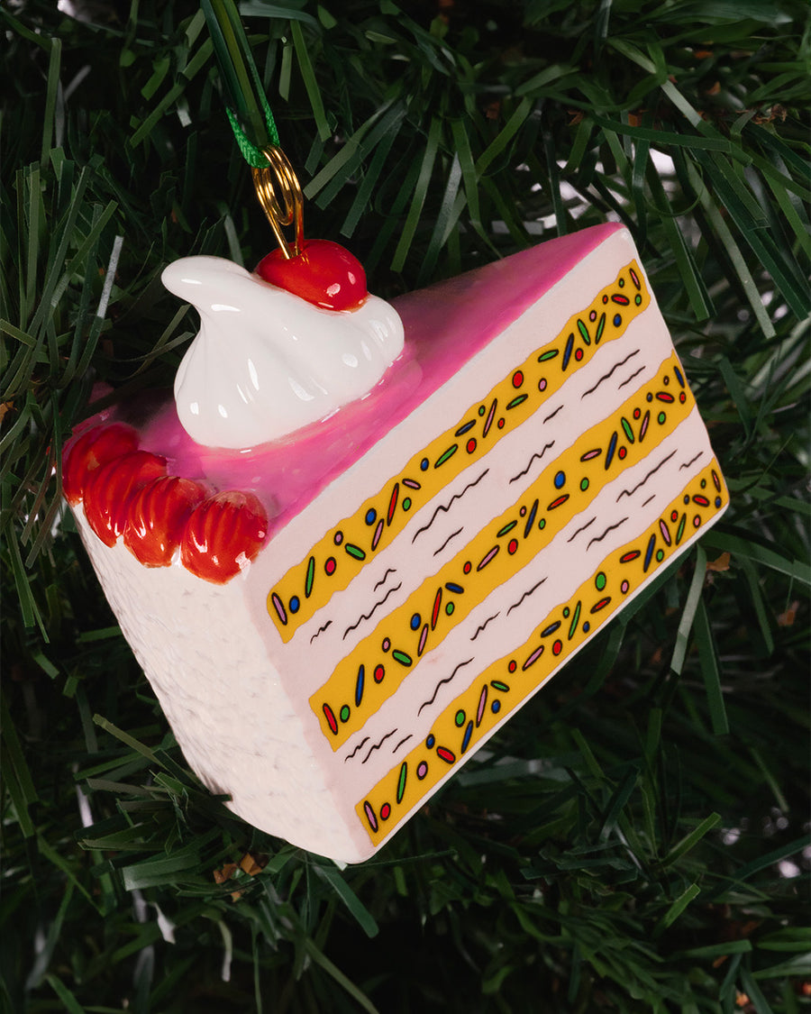 ceramic cake slice shaped ornament with sprinkle center and cherry and whipped topping on top on a tree