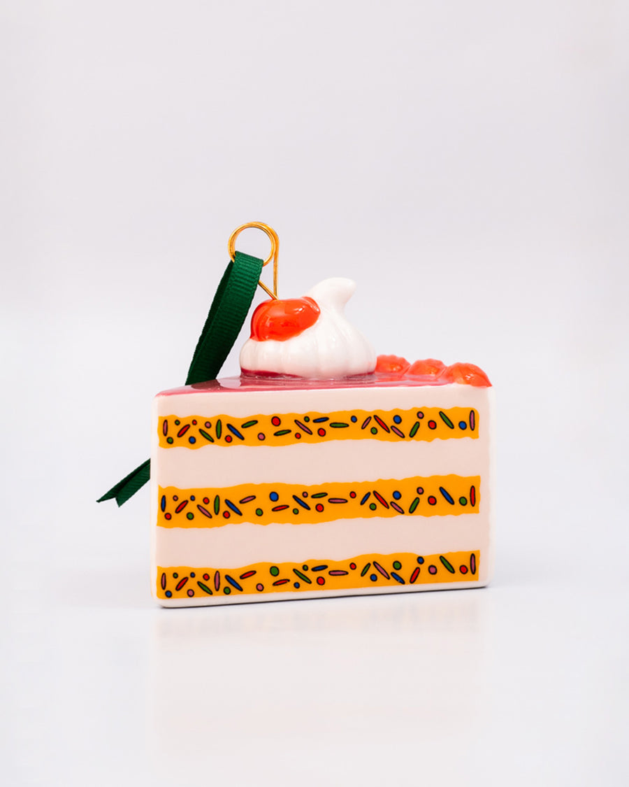 side view of ceramic cake slice shaped ornament with sprinkle center and cherry and whipped topping on top