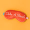 red satin eye mask with cursive 'take a break' across the front on orange background