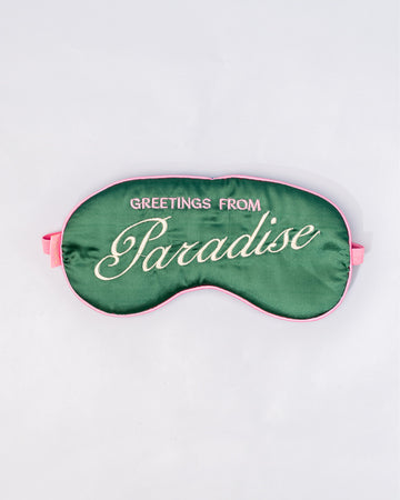 dark green sleep mask with pink and white embroidered 'greeting from paradise' with pink adjustable strap