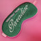 dark green sleep mask with pink and white embroidered 'greeting from paradise' with pink adjustable strap on a pink ground