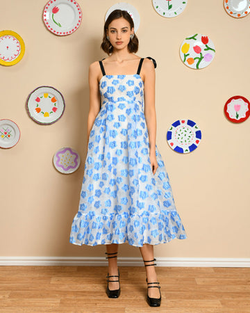 model wearing white/light blue midi dress with ruffle hem, black tie straps and all over blue flower print