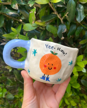 model holding white mug with periwinkle handle with 'yee-haw' orange on it