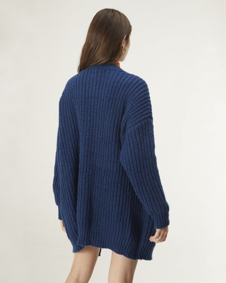 backview of model wearing oversized dark blue cardigan with orange top, white skirt and black boots