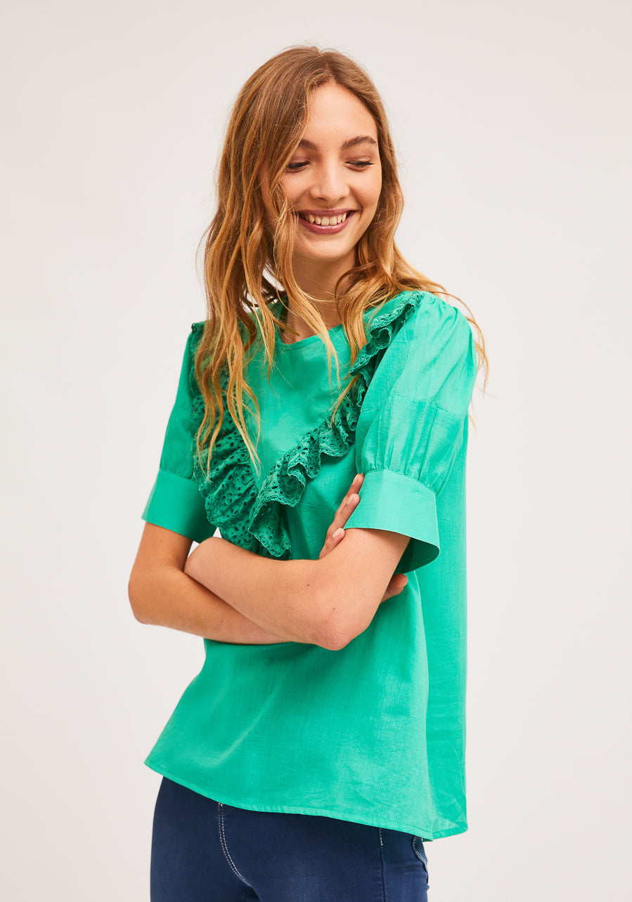 model wearing green ruffle-front blouse with eyelet detail and blue jeans