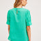 back view of model wearing green ruffle-front blouse with eyelet detail and blue jeans