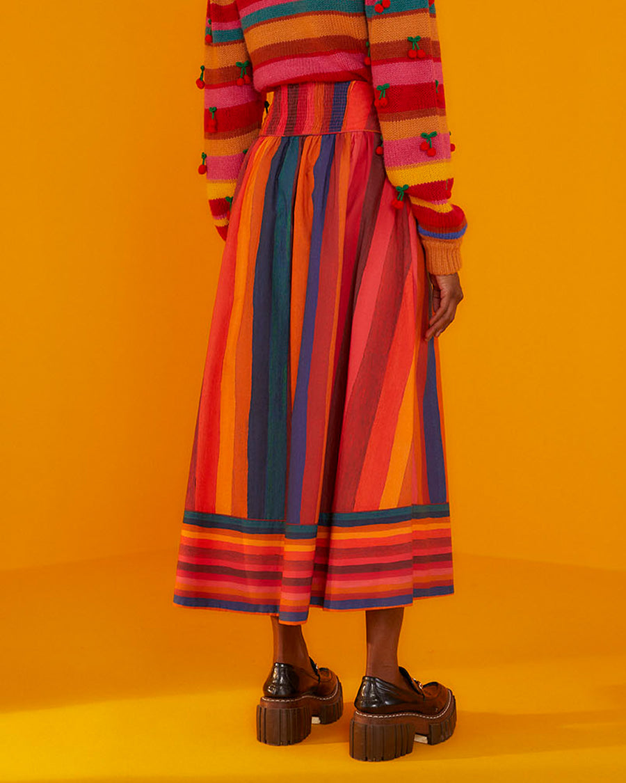 back view of model wearing multicolor vertical and horizontal stripe midi skirt with stripe cherry sweater and black platform shoes