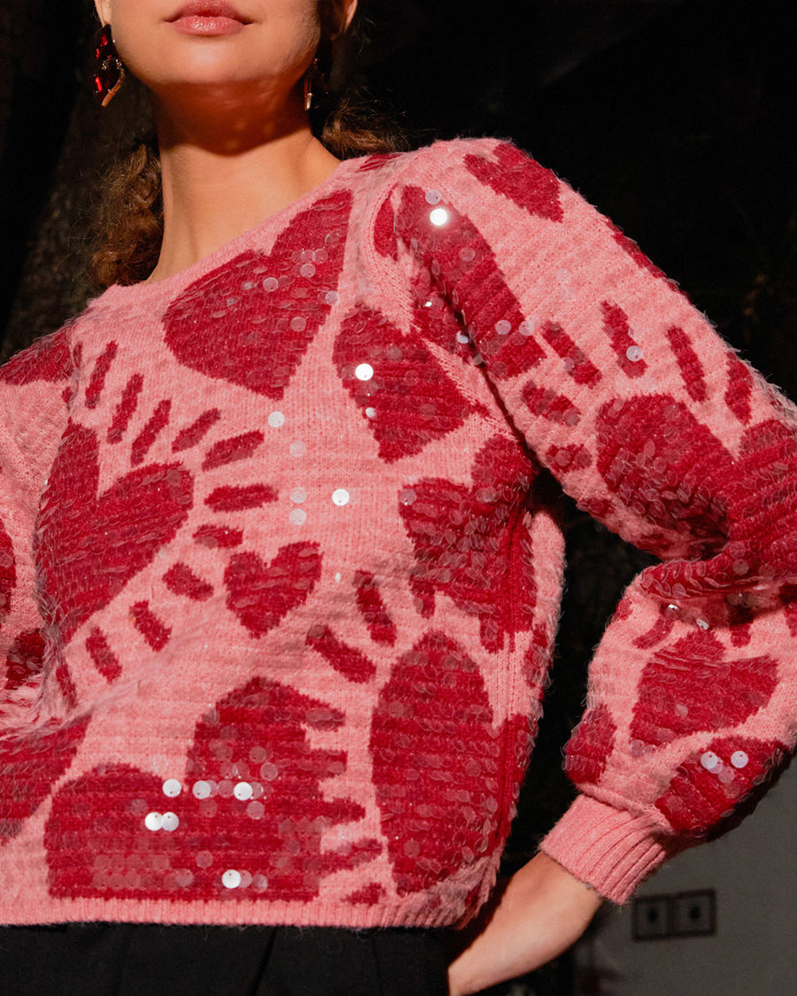 up close of model wearing pink cropped sweater with all over sequins and graphic heart print