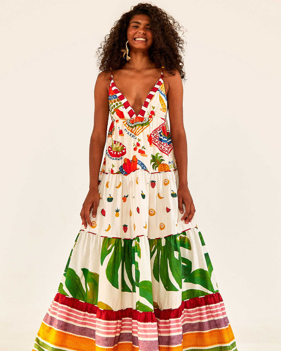 model wearing white maxi dress with various different multicolor prints, fruit charms on straps and deep v neckline