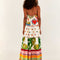 backview of model wearing white maxi dress with various different multicolor prints, fruit charms on straps and deep v neckline