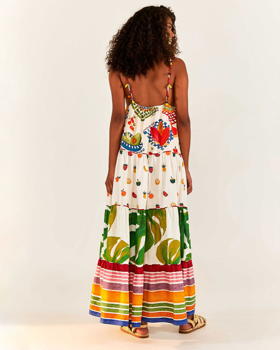 backview of model wearing white maxi dress with various different multicolor prints, fruit charms on straps and deep v neckline