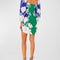 backview of model wearing blue and green linen mini dress with all over white floral print, square neckline and slight blouson sleeves