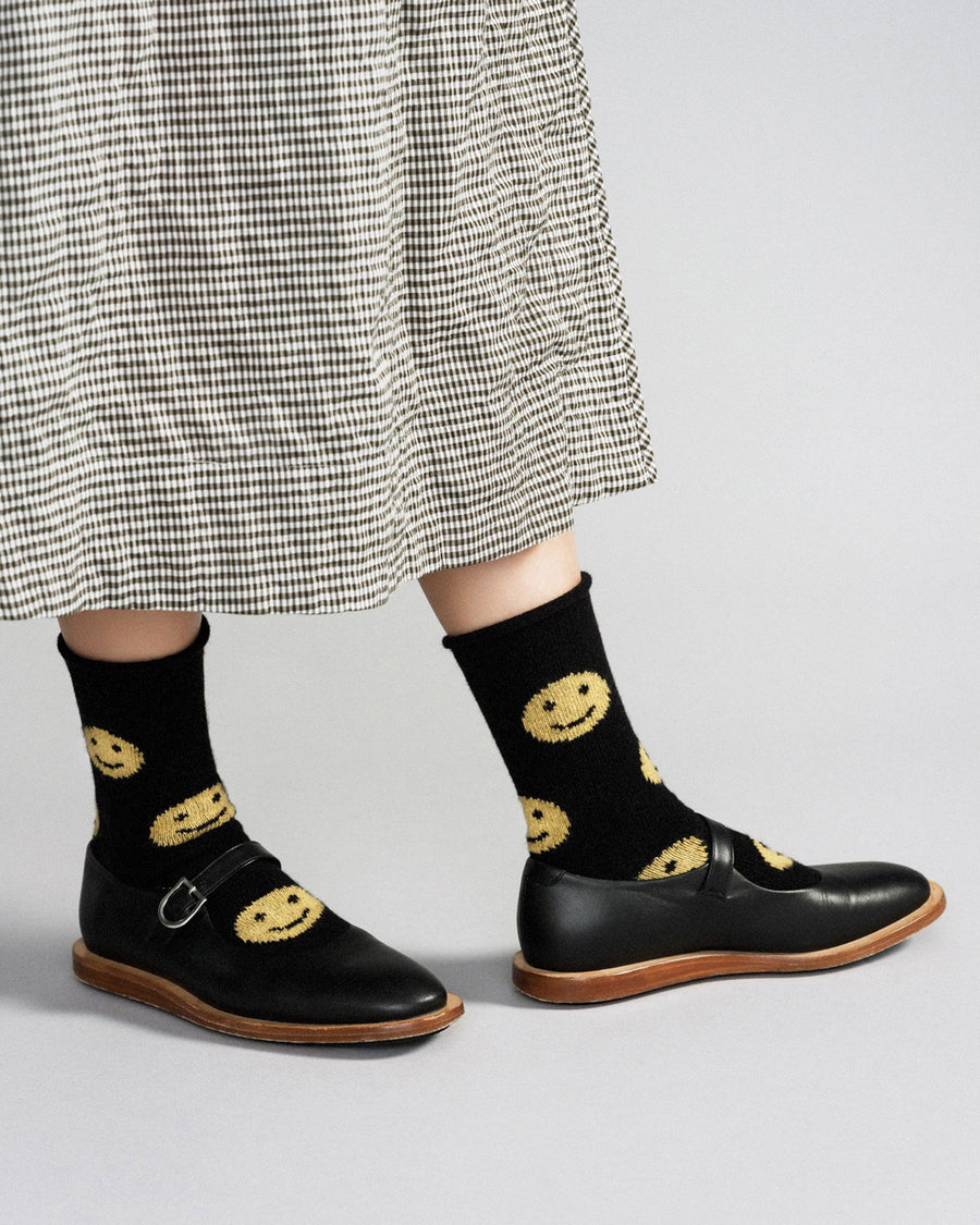 model wearing black crew socks with yellow happy faces all over with black mary jane shoes and black and white checkerboard print skirt