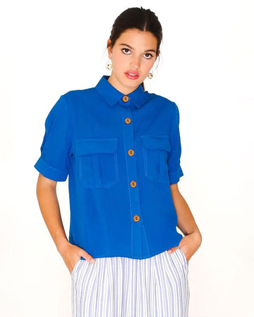 front view of model wearing royal blue button up short sleeve top with patch pockets on bust and brown buttons