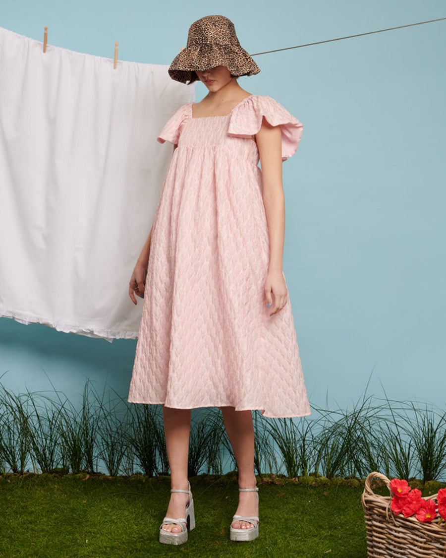 model wearing light pink flowy midi dress with flutter sleeves and textured flower design