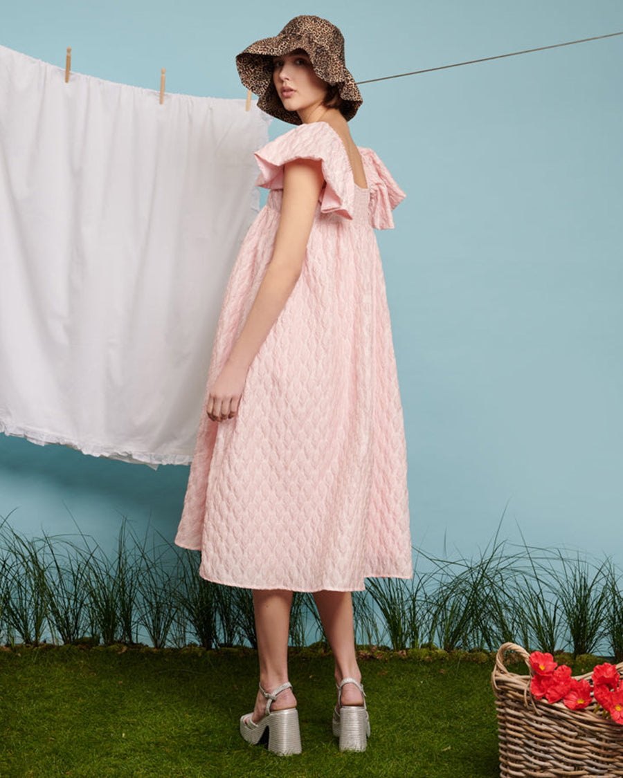 backview of model wearing light pink flowy midi dress with flutter sleeves and textured flower design