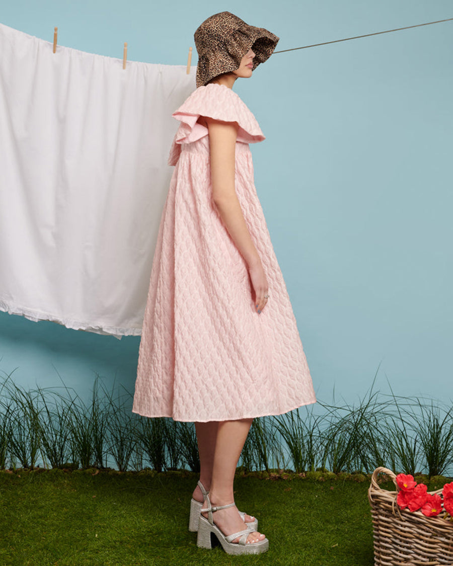 sideview of model wearing light pink flowy midi dress with flutter sleeves and textured flower design