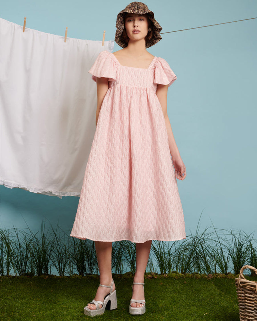 model wearing light pink flowy midi dress with flutter sleeves and textured flower design