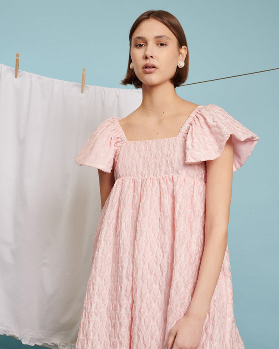 up close of model wearing light pink flowy midi dress with flutter sleeves and textured flower design