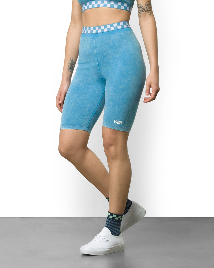 woman wearing blue bike shorts with blue and white checkerboard trim waistband and white shoes and black socks