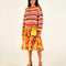 front view of model wearing yellow, orange, green, pink and red crochet stripe sweater, print skirt, lemon purse and strappy sandals