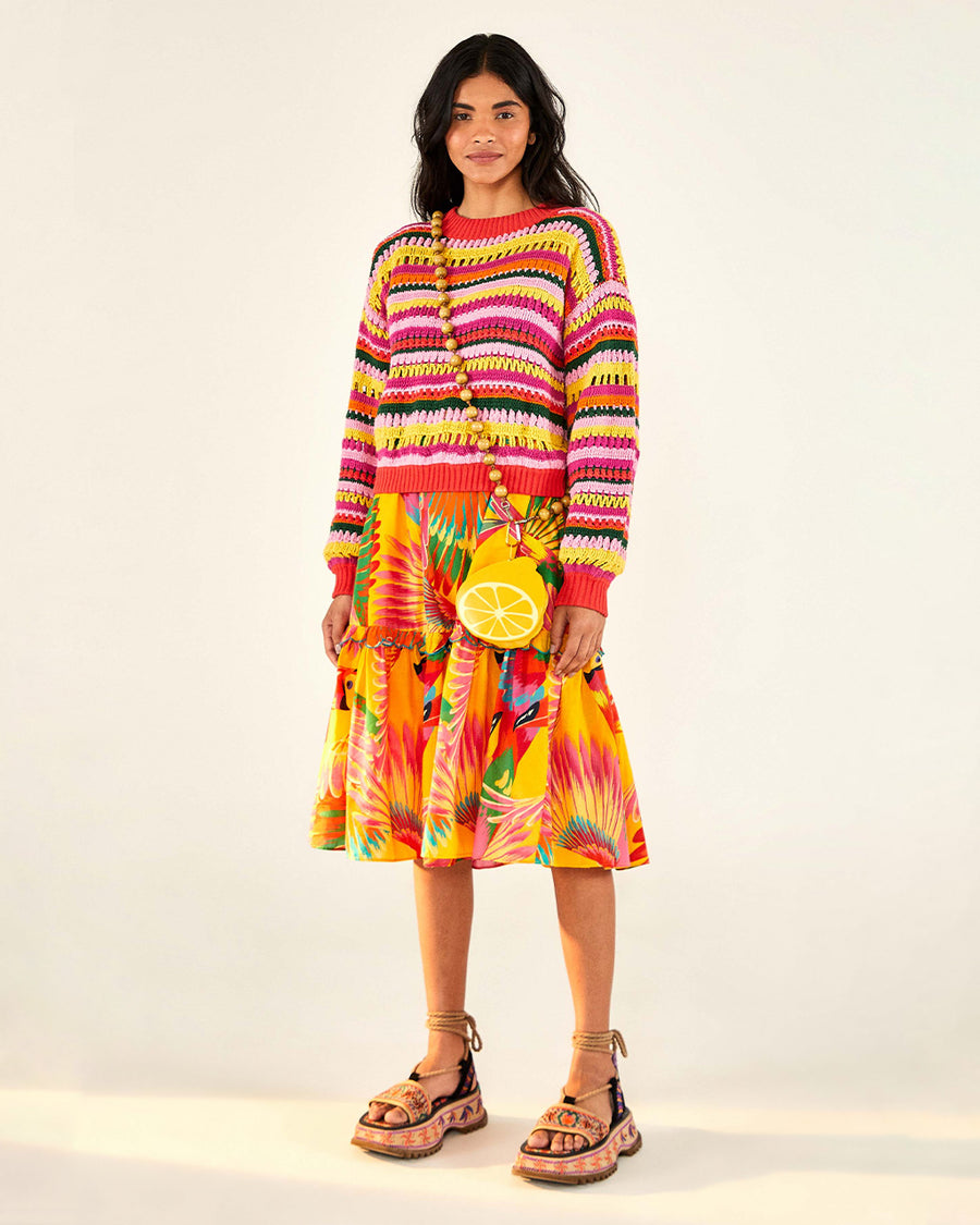 front view of model wearing yellow, orange, green, pink and red crochet stripe sweater, print skirt, lemon purse and strappy sandals