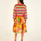 back view of model wearing yellow, orange, green, pink and red crochet stripe sweater, print skirt, and strappy sandals