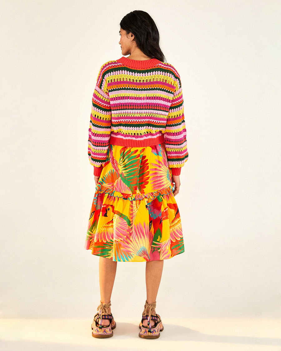 back view of model wearing yellow, orange, green, pink and red crochet stripe sweater, print skirt, and strappy sandals