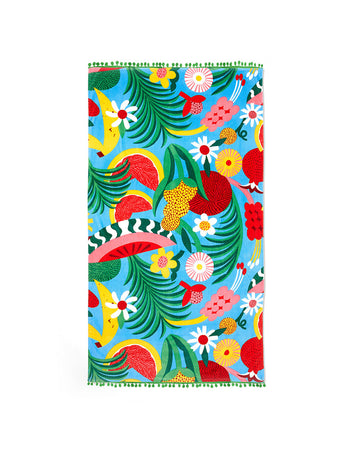 large beach towel with blue ground, abstract fruit print and green pom poms on each end