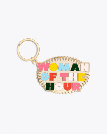 gold metal keychain with "WOMAN OF THE HOUR" text graphic in multicolor lettering