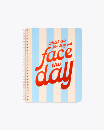 spiral bound notebook with blue and ivory striped pattern and "what do ya say we face the day" in metallic red text