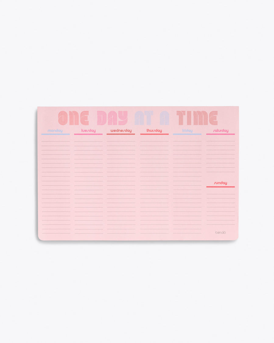 weekly deskpad in pink with "ONE DAY AT A TIME" text graphic at the top